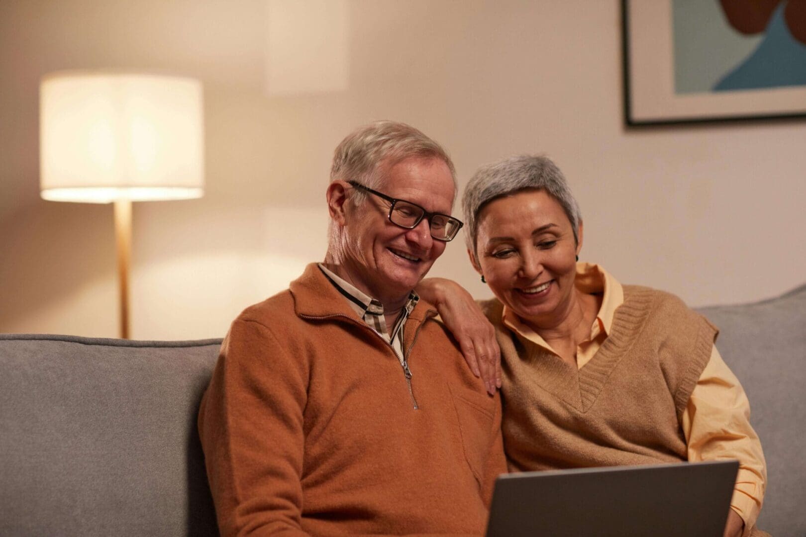 A man and woman sitting on the couch looking at a laptop.