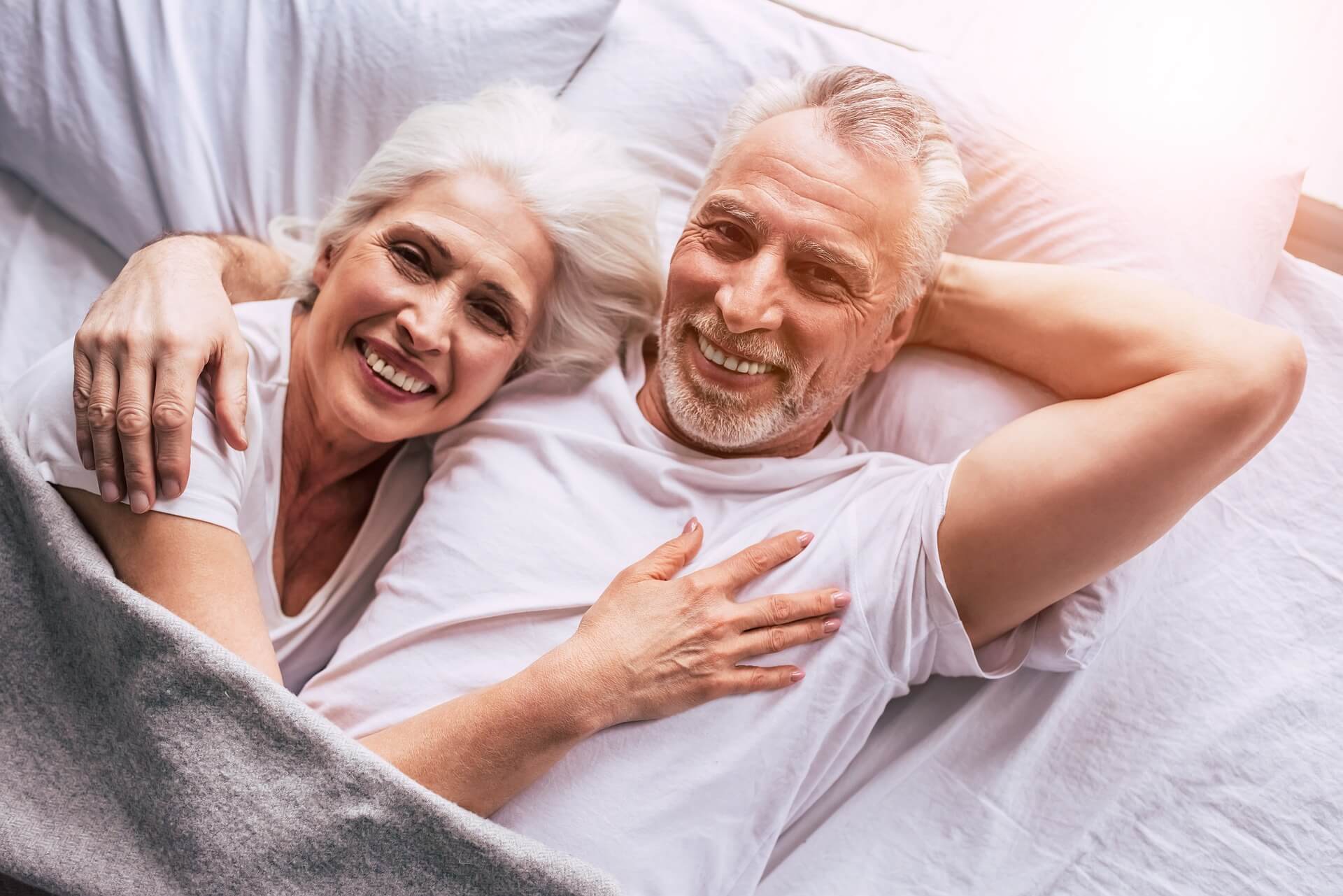 A man and woman laying in bed smiling.